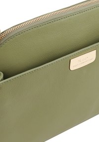 Lichtgroene leren pouch met een voorvak, gouden rits en een gouden merkplaat met het label "Paul Costelloe."
