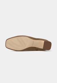 Sola de sapato de camurça marrom com bico quadrado, salto ligeiro, padrão de aderência sulcado e logotipo "Clarks" num fundo cinza claro.
