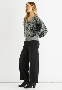 Grau leopardgemusterte Strickjacke mit V-Ausschnitt, oversized Passform und Knopfverschluss, kombiniert mit schwarzen weit geschnittenen Jeans und schwarzen hohen Stiefeln.