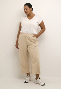 Pantalons beiges taille haute avec une coupe décontractée, en tissu texturé, assortis à un t-shirt blanc ajusté à col V et des baskets sportives.