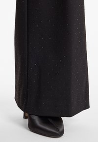 Zwarte stof met een gestippeld patroon en een subtiele glans, gecombineerd met een zwarte, puntige schoen van zachte satijn met een lage hak.