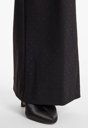 Zwarte stof met een gestippeld patroon en een subtiele glans, gecombineerd met een zwarte, puntige schoen van zachte satijn met een lage hak.