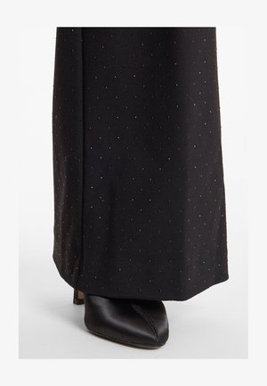 Zwarte stof met een gestippeld patroon en een subtiele glans, gecombineerd met een zwarte, puntige schoen van zachte satijn met een lage hak.