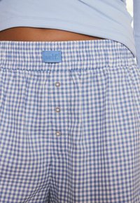 Shorts a cuadros de gingham en azul y blanco con una suave cintura elástica, que presentan una pequeña etiqueta azul y tres botones a presión plateados.