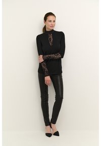 Black long-sleeve top featuring a lace neck and sleeve detail, paired with black faux leather pants and pointed black heels.