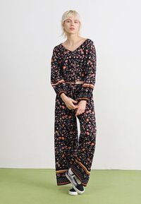 Ensemble deux pièces noir à fleurs avec manches longues et pantalons larges, ornés de motifs orange et verts aux poignets et à l'ourlet.