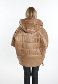 Braune Puffjacke mit großer Kapuze, gesteppter Textur und lockerem Schnitt, kombiniert mit schwarzen Leggings, von hinten betrachtet.