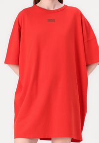 Czerwona, oversize sukienka t-shirtowa wykonana z bawełny, z okrągłym dekoltem i krótkimi rękawami. Na piersi znajduje się małe czarne logo.