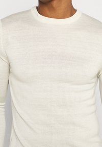 Ljusbeige stickad tröja med rund halsringning och långa ärmar. Tyget har en diskret textur och en figursydd design.