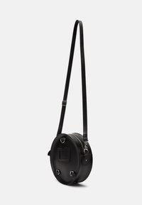 Čierna kruhová crossbody taška vyrobená z kože, s dlhým popruhom, striebornými kovovými detailmi a hladkým povrchom, na jednej strane s plochou vreckom.