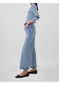 Haut à manches longues rayé bleu et blanc, jean large bleu clair, et chaussures plates noires, mettant en valeur une coupe décontractée et un style casual.