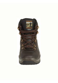 Brauner Wanderschuh mit Gummisohle, Lederoberteil, Metallösen und strukturiertem Zungenbereich mit einem Etikett, auf dem "Outdoor Adventure" steht.