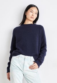 Marineblå strikkegenser med rund hals, lange ermer og avslappet passform, kombinert med lyseblå, svakt teksturerte jeans.