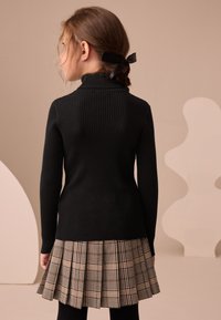 Ribstrikket sort sweater med høj krave kombineret med en plisseret, ternet nederdel i beige, brune og sorte farver. Enkel design med struktureret stof.