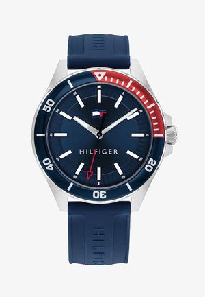 Merevaigistusega kella kummirihm; ümmargune kellanäidik sisaldab valgeid tunni märke, punaseid ja siniseid aktsente ning Hilfigeri logo.