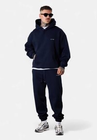 Navyblaues Hoodie- und Jogginghosen-Set aus weichem Material. Das Hoodie hat eine Kängurutasche und ein Logodesign. Die Hose hat einen verstellbaren Bund.