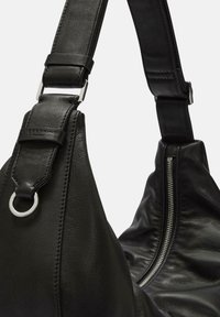 Borsa a spalla in pelle nera caratterizzata da una forma curva distintiva, texture flessibile, zip visibile e tracolla regolabile con hardware in metallo.