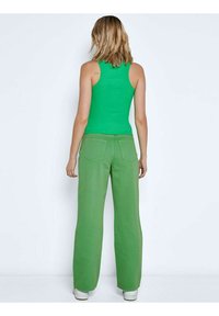 Zelený bezramenný top spojený s širokými zelenými kalhotami. Oba kusy jsou vyrobeny z hladké látky. Boty jsou bílé s nízkým profilem.