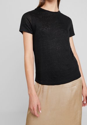 T-shirt nero a maniche corte realizzato in tessuto leggero e leggermente trasparente. Collo rotondo con vestibilità morbida, indossato sopra una gonna in satin beige.