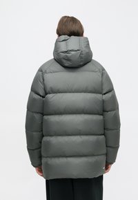 Casaco puffer cinza com capuz destacável, design acolchoado e grandes secções. O tecido tem uma textura suave com um estilo minimalista.