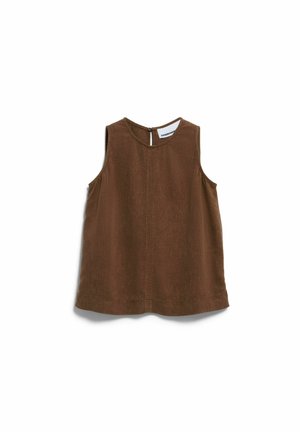 Femme aux cheveux courts et bouclés portant un haut marron sans manches et un short marron assorti, debout devant un fond blanc uni.