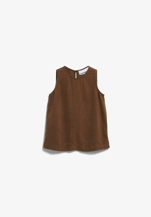 Femme aux cheveux courts et bouclés portant un haut marron sans manches et un short marron assorti, debout devant un fond blanc uni.