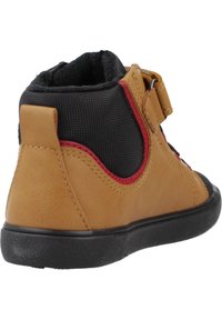 Bota de tobillo de cuero marrón con paneles de tela negra, acentos rojos y una correa de gancho y bucle. Suela de goma resistente y acabado texturizado.
