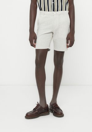 Jasnoszare, lniane spodenki o dopasowanym kroju, z bocznymi kieszeniami i zapięciem na guzik. W zestawie z ciemnobrązowymi skórzanymi butami.