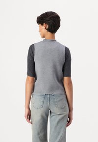 Top grigio a maglia senza maniche con collo rotondo, abbinato a maniche corte scure, indossato con jeans chiari a vita alta.