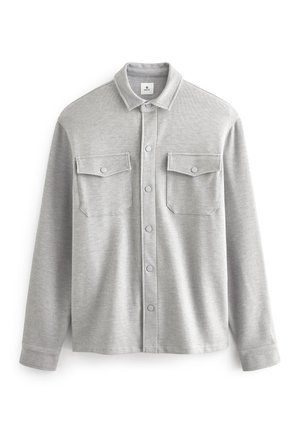 Chemise gris clair à manches longues avec col et deux poches devant à rabats avec boutons, en tissu doux texturé.