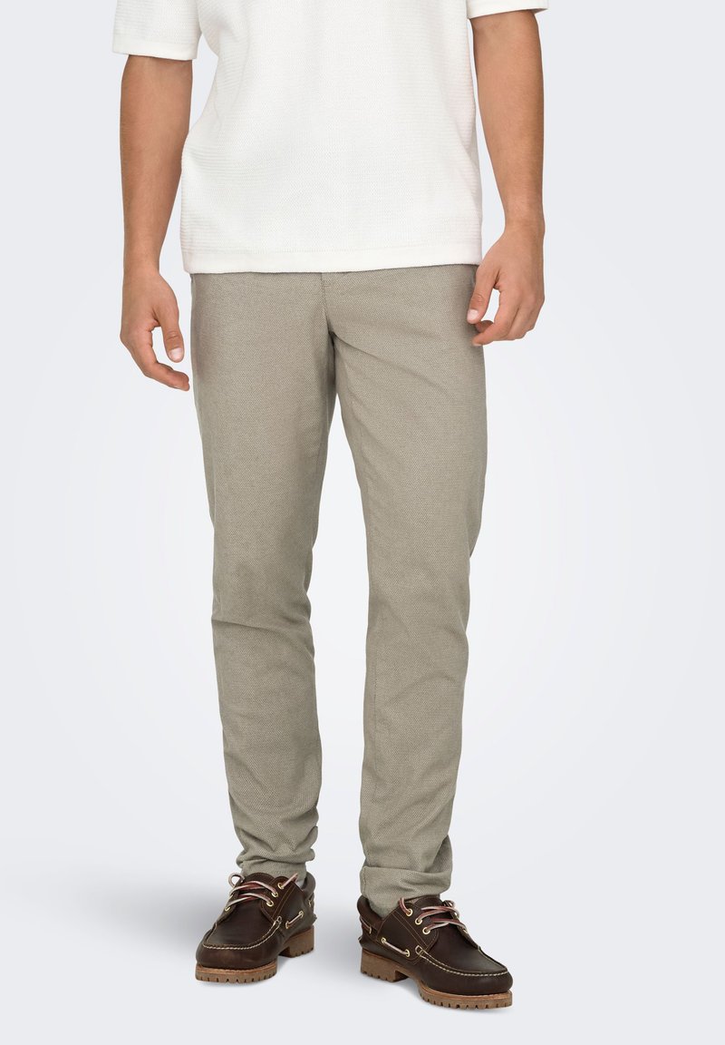 Pantalon gris clair texturé à coupe slim, associé à des chaussures marron à lacets avec une semelle contrastante et des lacets roses.