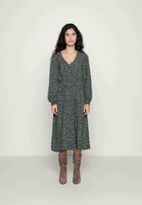 Μακρυμάνικο ναυτικό φόρεμα με λουλούδια και V-λαιμόκοψη, διαθέτοντας φαρδύ φούστα και ραμμένα μανίκια. Συνδυασμένο με ανοιχτό καφέ μπότες μέχρι το γόνατο.