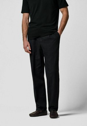 Zwarte linnen broek met een rechte pasvorm, voorzien van zijzakken en een tailleband. Gecombineerd met donkere schoenen en een zwart shirt met korte mouwen.