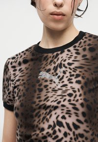 Γυναίκα που φοράει πουκάμισο με λεοπάρ σχέδιο, μαύρο γιακά και άκρες στα μανίκια, με λογότυπο πάνθηρα από στρας στο στήθος.