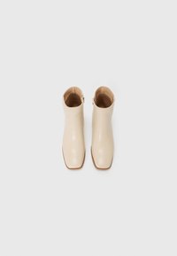 Bottines en cuir beige à bout carré, texture lisse et fermeture éclair sur le côté. La semelle présente un accent marron clair.