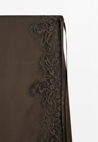 Dark brown fabric with intricate floral lace trim along one edge and a narrow matching strap beside it on a light background.