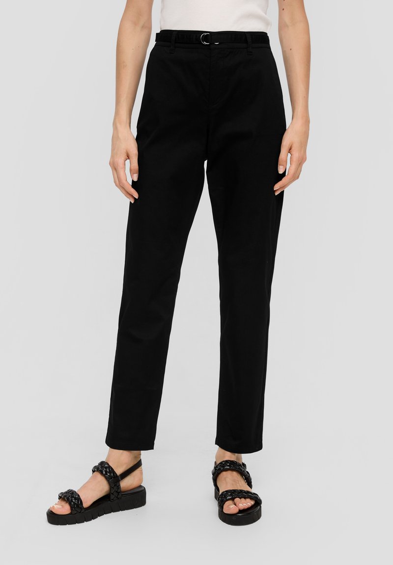 Zwarte katoenen broek met een relaxte pasvorm, voorzien van een riem met een metalen gesp. Model draagt zwarte gevlochten sandalen met een dikke zool.