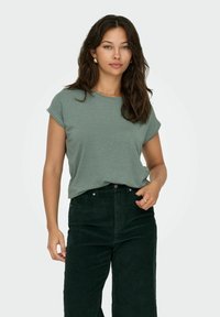Top verde a maniche corte con una texture sottile, abbinato a pantaloni in velluto a coste verde scuro a vita alta, con un classico design a cinque tasche.