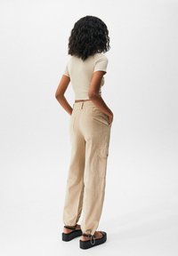 T-shirt beige court à manches courtes associé à un pantalon cargo beige clair avec poches latérales, taille élastique et bas resserrés.