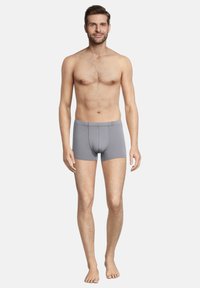 Boxer in cotone elasticizzato grigio con un design aderente, caratterizzati da una vita liscia e senza cuciture visibili. Il modello sta in piedi a piedi nudi, rivolto in avanti.
