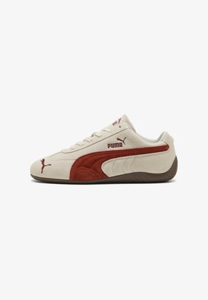 Niskoprofilowe beżowe zamszowe buty sportowe Puma z czerwoną zamszową paską, brązową podeszwą i logo Puma na boku i języku.