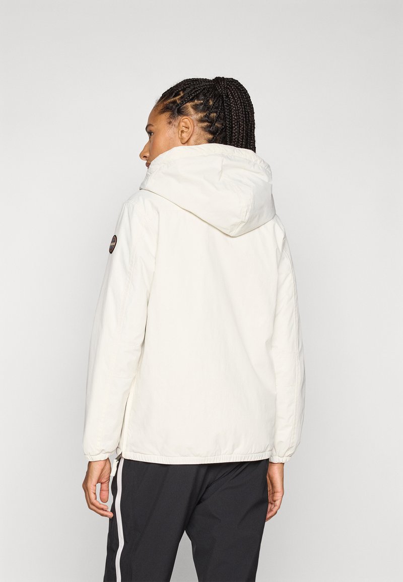 Chaqueta blanca ligera con capucha, mangas raglán, puños elásticos y un parche de logo en el costado. Textura suave y ajuste relajado.