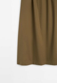 Tissu marron drapé avec des plis subtils contre un fond blanc, montrant la partie inférieure d'un vêtement.