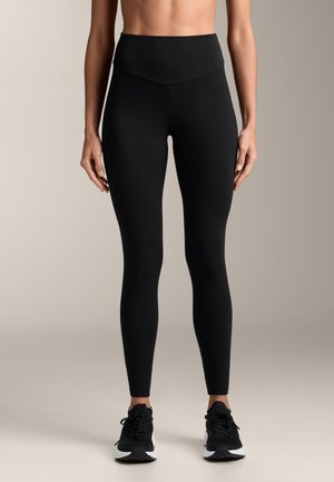 Schwarze hochgeschnittene Leggings aus einem glatten, dehnbaren Material mit passgenauer Silhouette, kombiniert mit schwarzen Sportschuhen.