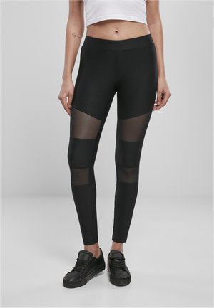 Leggings noirs à côtes avec des panneaux en maille transparente au milieu de la cuisse. Design taille haute avec une forme ajustée. Associés à des baskets noires.
