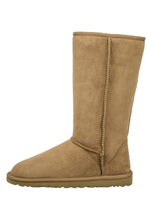 Hohe beigefarbene Wildlederstiefel mit flacher Gummisohle, gesteppten Nähten und glatter Textur. Entwickelt für Wärme und Komfort.