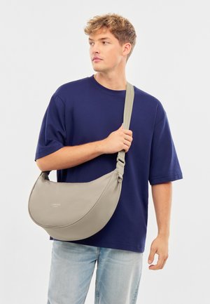 Šedá hobo taška vyrobená z hladkého materiálu, s zakriveným tvarom, nastaviteľným popruhom a detailom loga v minimalistickom dizajne.