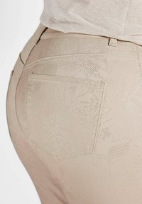 Jeans beige con un motivo floreale testurizzato e accenti a pois. Presentano una tasca posteriore e un design aderente. Il materiale sembra liscio.
