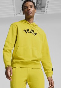 Gul hoodie i mjukt material, med en svart broderad "PUMA"-logotyp, en framficka och ribbade ärmslut med kontrasterande kant.