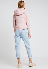 Lys pink polstret jakke med hætte, med stiksyninger i kanalerne. Parret med lyseblå opfoldede jeans og sneakers i neutrale farver.